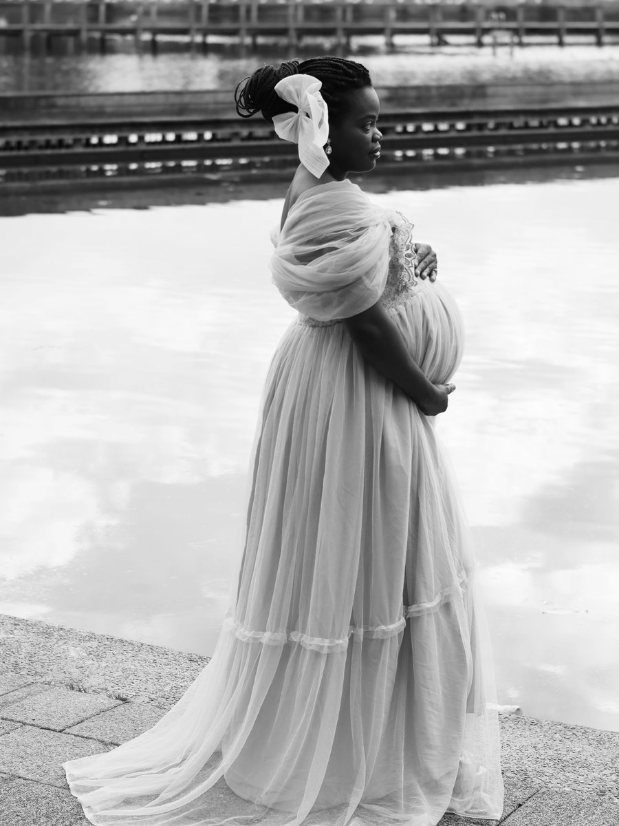 Mum, heavily pregnant, standing by the water in a flowing gown